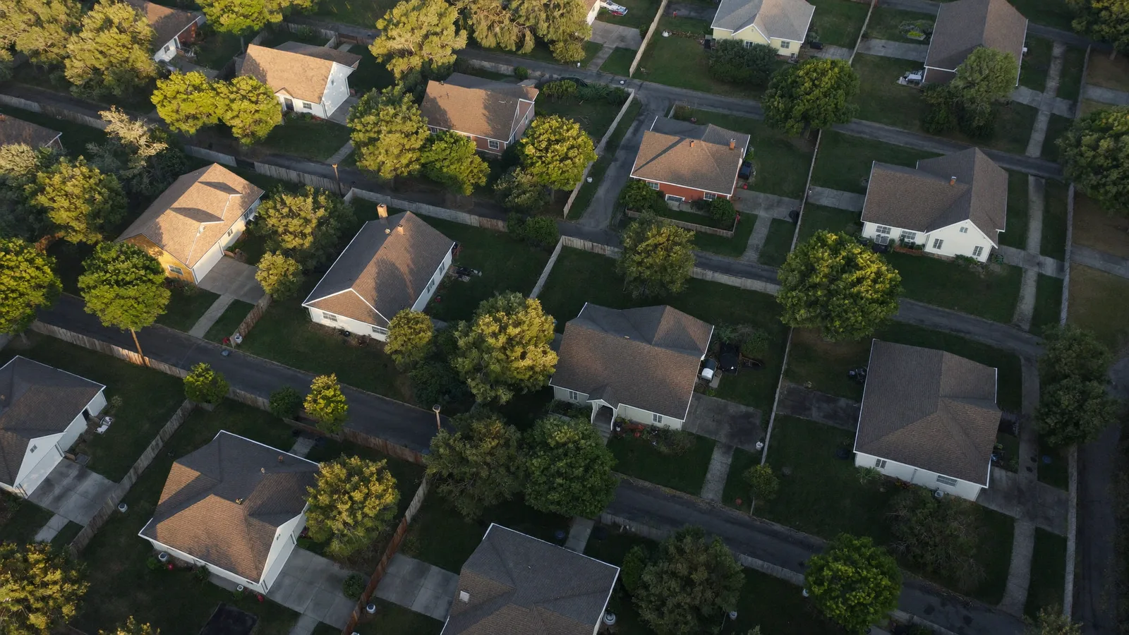 Aerial view over an established suburban neighborhood of detached houses on wooded lots in late afternoon light